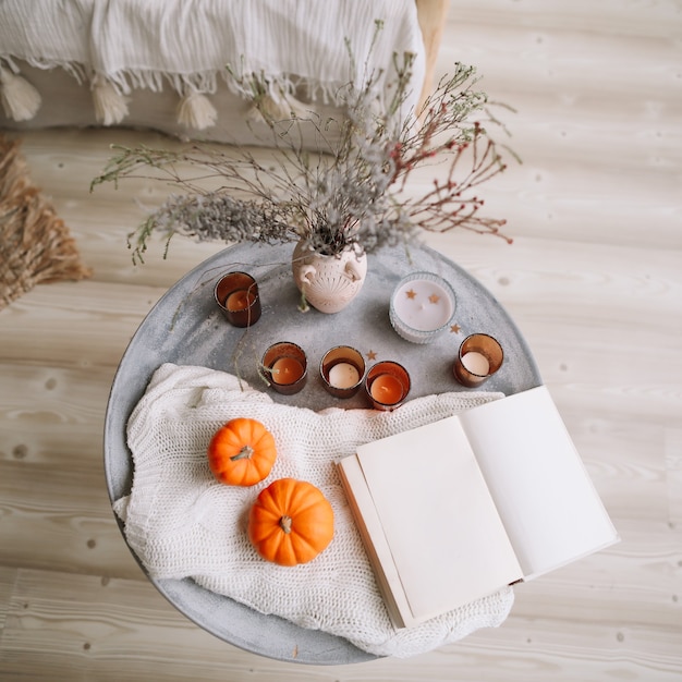 Herbstkomposition mit Kürbiskerzenbuch und getrockneten Blumen mit warmem Plaid