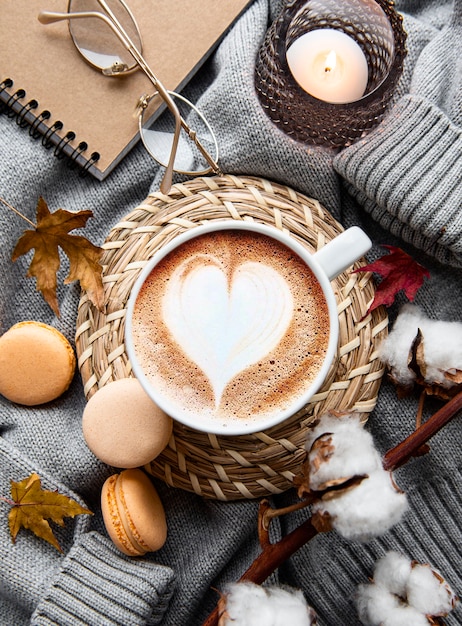 Herbstkomposition mit Tasse Kaffee, warmer Decke, dekorativen gestreiften Kürbissen, Kerzen und Herbstlaub