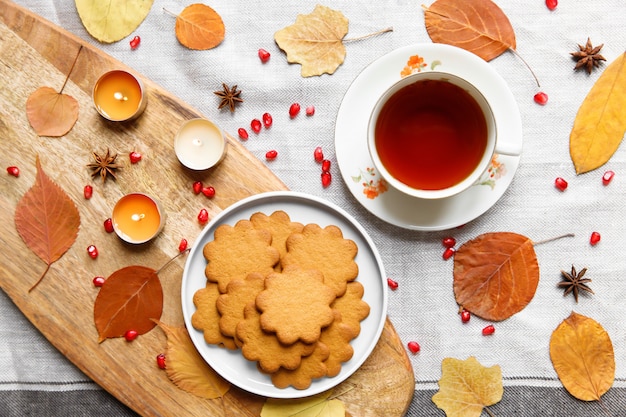 Herbstkomposition. Tasse heißen Tee, Lebkuchen, brennende Kerzen, gelbe Laubblätter, Samen Granatapfel, Anis auf einer Leinentischdecke