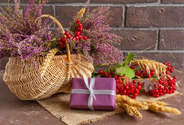 Herbstkomposition von Heidekraut in einem Weidenkorb Viburnum Weizenähren und Geschenken Stillleben