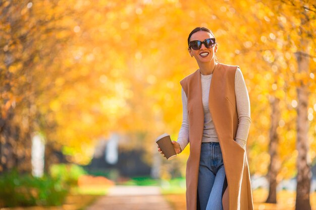 Herbstkonzept - schöne Frau, die Kaffee im Herbstpark unter Herbstlaub trinkt