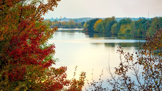 Herbstlandschaft mit Fluss und bunten Bäumen am Abend