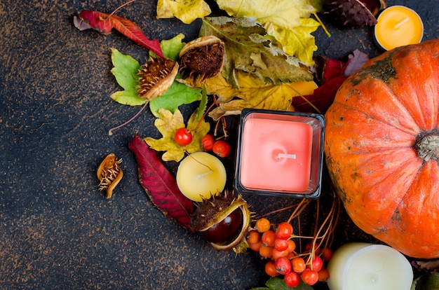 Herbstlaub, Kürbis, Kastanien, Kerzen auf einem dunklen Hintergrund