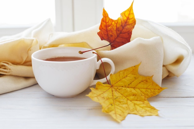 Herbstlaub mit einer Tasse Tee oder Kaffee neben einem Schal auf Holzhintergrund mit Kopierraum