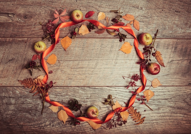 Foto herbstliche anordnung von blättern, äpfeln und beeren auf einem hölzernen hintergrund mit freiem platz für text. draufsicht, saisonkonzept, getönter retro-effekt