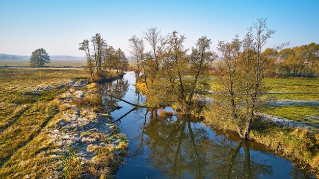 Foto herbstliche ländliche landschaft frost gras fluss grünes feld wiese bäume flussufer schmutzstraße grasland