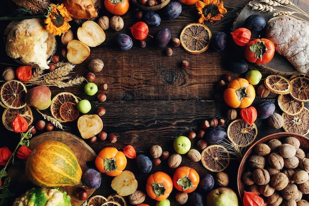 Herbstliche Stillleben-Komposition mit frischem Obst und Gemüse Sortiment von Pflaumen, Kaki, Kürbissen, Äpfeln, Walnuss, Sonnenblumen und trockenen Orangen auf rustikalem Holztisch, Draufsicht, Kopierraum