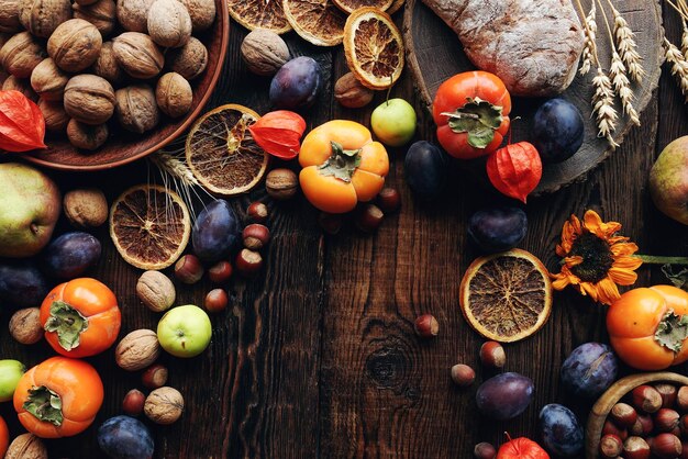 Herbstliche Stillleben-Komposition mit frischem Obst und Gemüse Sortiment von Pflaumen, Kaki, Äpfeln, Walnuss, Sonnenblumen und trockenen Orangen auf rustikalem Holztisch, Draufsicht, Kopienraum