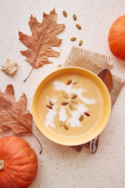 Herbstliche vegane gesunde Kürbiscremesuppe mit pflanzlicher Sahne und Samen zwischen Herbsteichenblättern und Kürbissen Draufsicht Essen