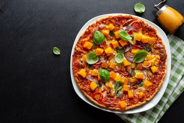 Herbstliche vegetarische Pizza mit Kürbis und Gemüse auf dunklem Hintergrund.