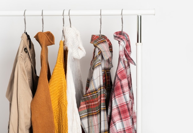 Herbstliche Vintage-Kleidung hängt auf Kleiderbügeln am Regal. Beige Trenchcoat, Pullover, karierte Hemden. Raumorganisation, Winterreinigung
