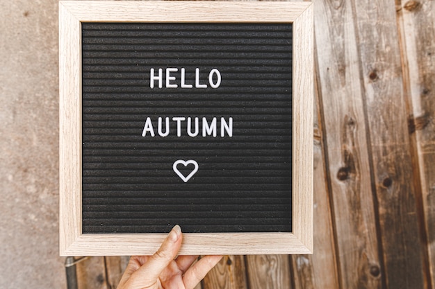 herbstlicher Hintergrund. Hand, die schwarzes Buchstabenbrett mit Text hallo Herbst hält