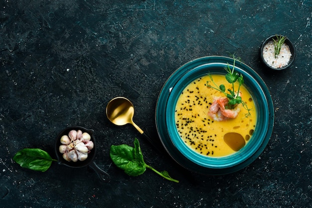 Herbstmenü Kürbissuppe mit Garnelen-Olivenöl und Sesamsamen In einer blauen Schüssel Auf schwarzem Steinhintergrund