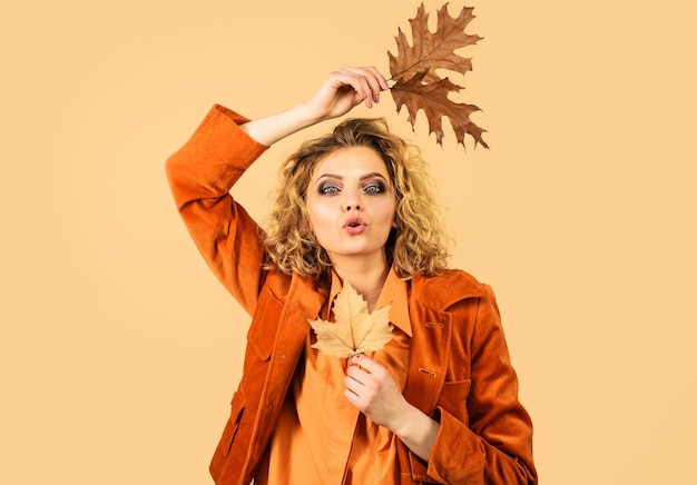 Herbstmodemädchen mit Herbstlaub sinnliche Frau in orangefarbener Jacke sendet Luftkuss