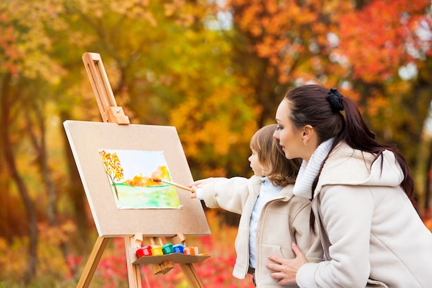 Herbstnatur, Mutter und Tochter malen ein Bild in einem Park aus Herbstblättern, malen ein kleines Kind, Kinderkreativität.