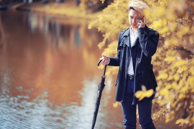 Herbstpark bei Regenwetter und ein junger Mann mit Regenschirm