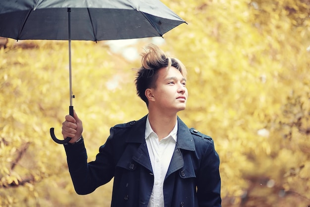 Herbstpark bei regenwetter und ein junger mann mit regenschirm