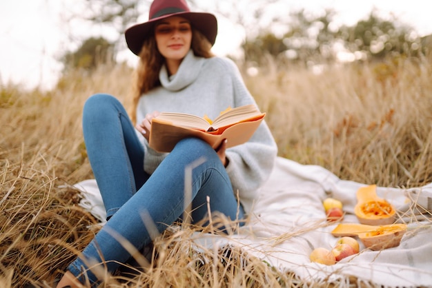 Herbstpicknick in der Natur Junge Frau sitzt auf der Decke, liest ein Buch und lächelt im Freien