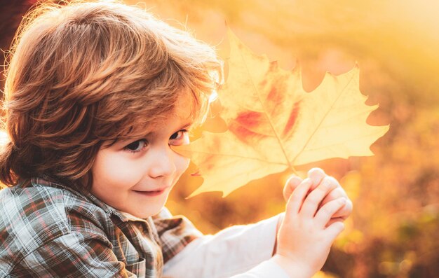 Herbstporträt eines süßen kleinen Jungen, Nahaufnahme von Kindern, die mit Blättern im Herbstpark spielen