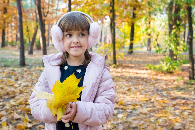 Herbstporträt im Freien eines glücklichen Kindes mit Ahornblättern im Park an einem sonnigen Tag