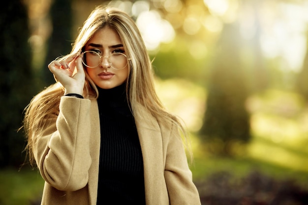 Herbstporträt. Stilvolle Frau in Bildbrille und Mantel im Park