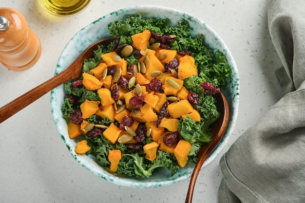 Herbstsalat mit Grünkohl, geröstetem Kürbis, Samen und getrockneten Preiselbeeren in Schüssel. Grauer Hintergrund. Attrappe, Lehrmodell, Simulation. Ansicht von oben.