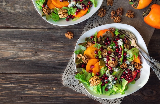 Herbstsalat mit Kaki, Granatapfel, Blauschimmelkäse und Walnüssen auf rustikalem Holztisch. Draufsicht.