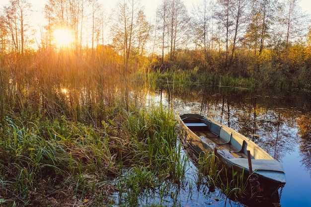 Foto herbstsonnenuntergang auf dem fluss mit einem boot im vordergrund