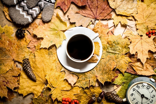 Herbststil. Tasse Kaffee mit Wecker auf Herbstlaub.