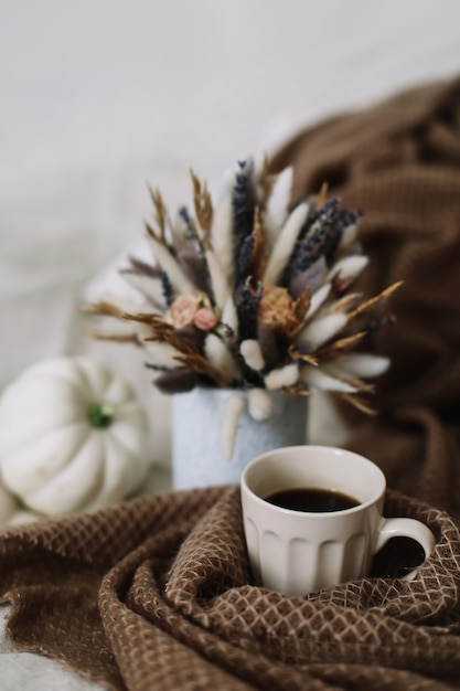 Herbststillleben mit einer Kaffeetasse mit Blumen und Kürbissen auf einem gemütlichen Plaid