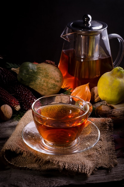 Herbststillleben mit Glasteekanne und Tasse Tee auf Sackleinen