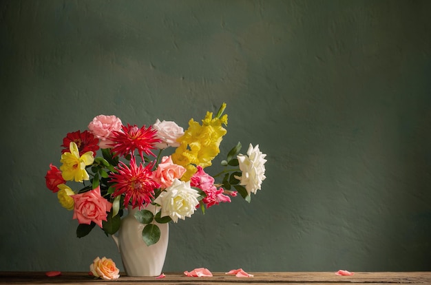 Herbststrauß mit roten und gelben Blumen in weißer Vase auf dunklem Hintergrund