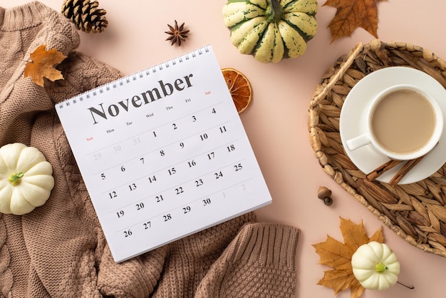 Herbstwärme in einem Schnappschuss Top-View-Komposition Kalender gestrickter brauner Pullover heißer Kaffee in Wickelkorb Pattypanen Eichel Zimt Ahornblätter Pinienkegel getrocknetes Orange auf weichem beige Hintergrund