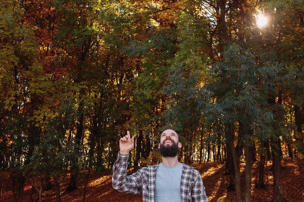 Herbstwald Fröhlicher Hipster-Typ, der im Naturpark mit dem Finger nach oben in die Luft zeigt Herbstbäume Hintergrund