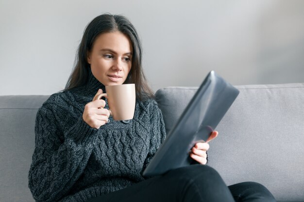 Herbstwinterporträt des jungen Mädchens mit digitaler Tablette und Schale des heißen Getränks