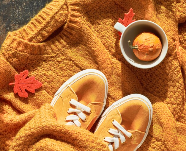 Herbstwohnung lag mit gelbem Pullover, dekorativem Kürbis in Teetasse und Herbstlaub