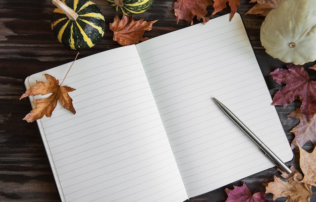 Herbstzusammensetzung Kürbisse und Blätterrahmen mit Notizbuch auf hölzernem Hintergrund