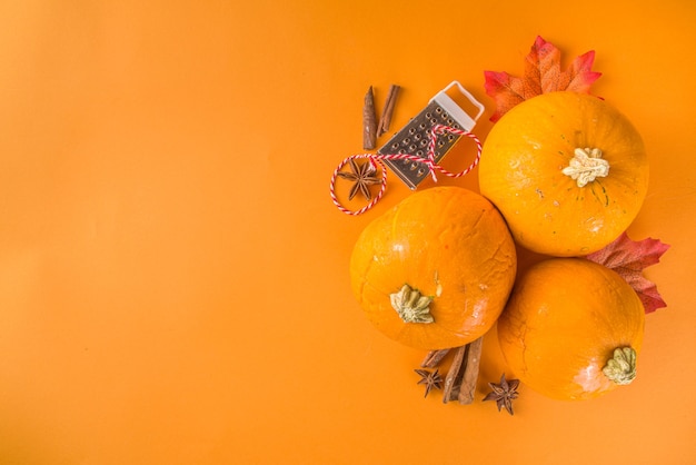 Herbstzusammensetzung, Thanksgiving-Feiertag-Grußkarte. Kürbiskochhintergrund, mit festlichem Herbstdekor, kleinen Kürbissen, Gewürzen, Pekannüssen, trendigem buntem orangefarbenem Hintergrundkopierraum