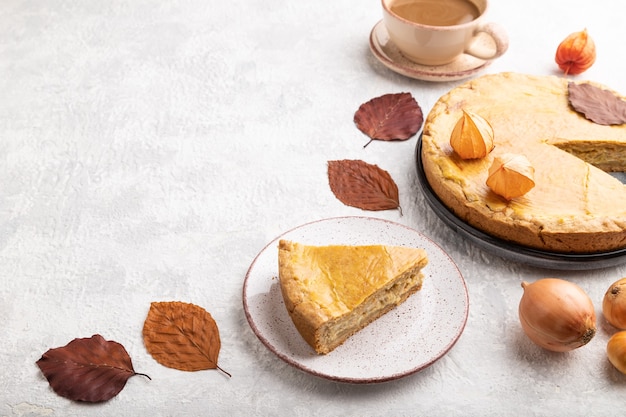 Herbstzwiebeltorte verziert mit Blättern und Tasse Kaffee auf grauem Beton