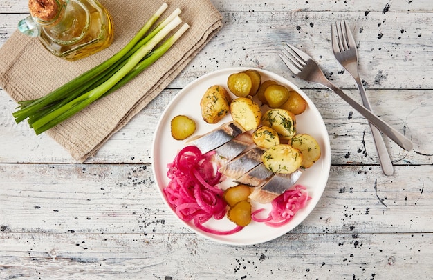 Foto hering mit gebackenen kartoffelzwiebeln und eingelegter gurke im flatlay