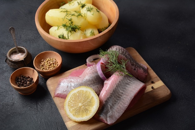 Heringsfilet auf Holzbrett mit Pfefferkräutern, roten Zwiebeln und Zitrone