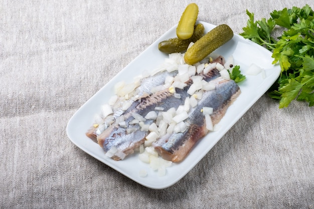 Heringsfilet mit Zwiebel auf einem weißen Teller und grauem strukturiertem Hintergrund.