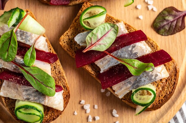 Heringsfilet Sandwich mit gesalzenem Hering Scheibe rote Beete grüne Gurke Zwiebel und Microgreen auf den Toasts skandinavische Küche Tradition dänisches offenes Sandwich Draufsicht