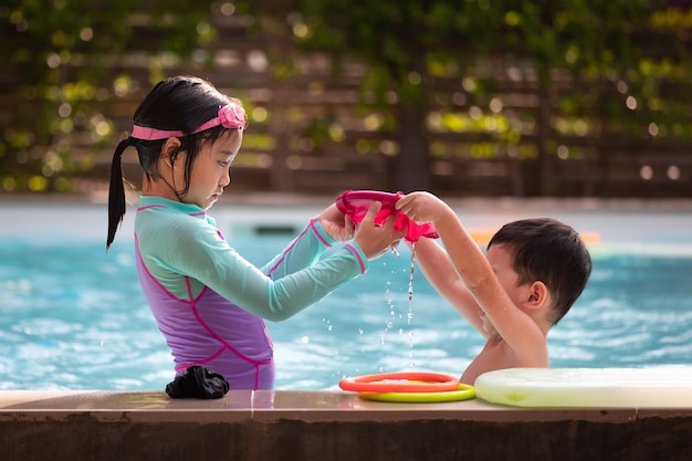 Hermana asiática niña y niño jugando agua con juguetes juntos en la piscina con diversión. Actividad de verano y concepto de estilo de vida infantil.