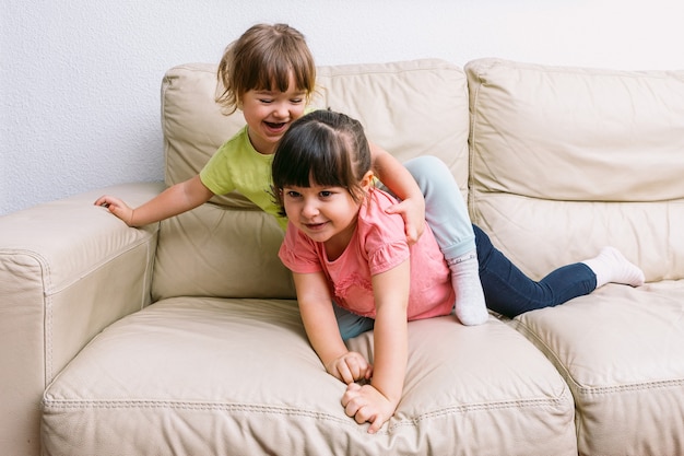 Hermana de dos niñas abrazado, acostado en un sofá jugando
