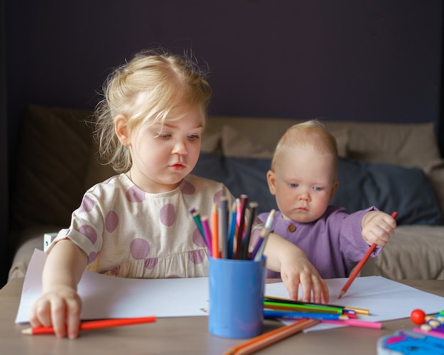 Hermana de dos niños y hermano de niño dibujo con lápices juntos en casa