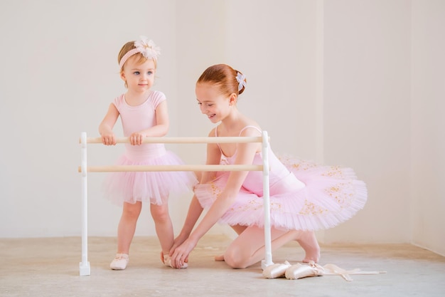 Foto la hermana mayor, una bailarina con un tutú rosa y zapatillas de punta, le muestra al bebé cómo practicar en la barra.