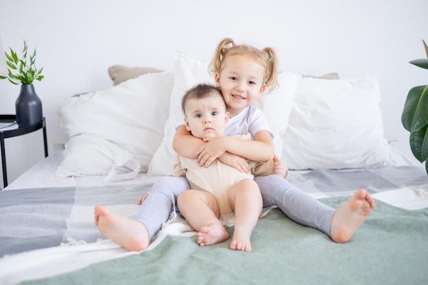 La hermana mayor sostiene y abraza al bebé en casa en la cama el amor y la amistad de las hermanas en la familia