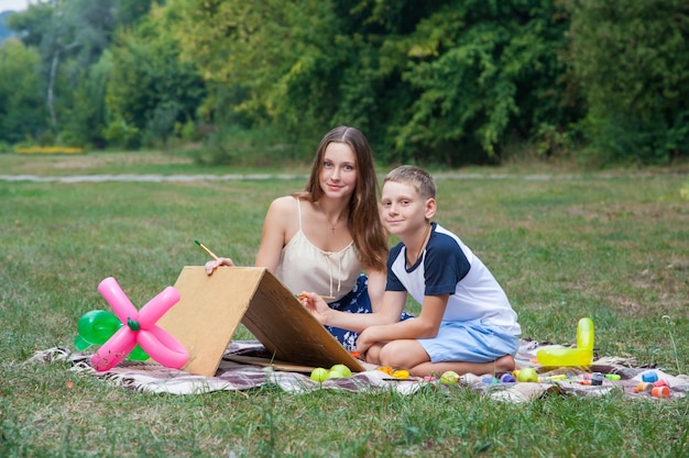 Hermana mayor tratando de enseñar a su hermano a pintar en el parque