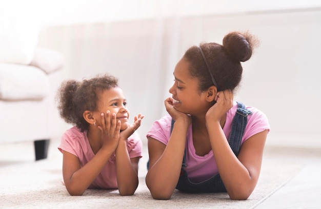 Hermanas afro juguetonas tiradas en el suelo y sonriendo entre sí